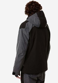 Giacca con cappuccio nera e grigia con un motivo texture, caratterizzata da pannelli delle spalle a contrasto e cappuccio regolabile. Il tessuto sembra resistente alle intemperie.