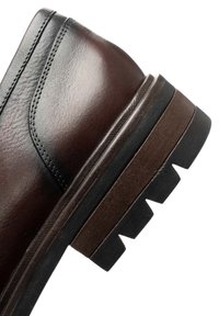 Donkerbruin lederen schoenhiel met zwart en bruin gegroefd zool en gedetailleerde stiksels op het leren bovenwerk.