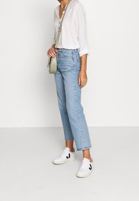 Leichtes weißes Hemd mit dezenten Punkten, hochtaillierte, hellblaue Jeans und weiße Sneakers mit schwarzen Akzenten. Kleine Umhängetasche inklusive.