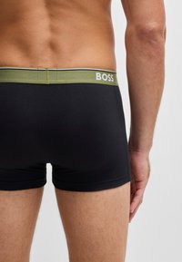 Fekete boxer alsónadrág elasztikus anyagból, zöld derékpánttal, fehér "BOSS" márkajelzéssel, látható varrással és szoros illeszkedéssel.