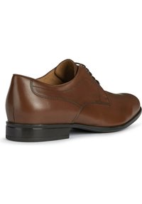 Chaussure habillée en cuir marron avec une finition lisse, bout arrondi et un système de laçage. Présente une semelle en caoutchouc noir et des accents de couture subtils.