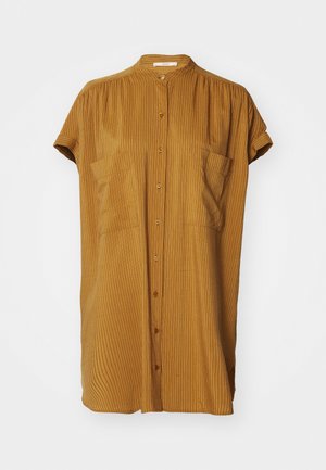 Chemise à boutons jaune moutarde, col mandarin, manches courtes retroussées et texture à côtes verticales. Deux poches à l'avant.