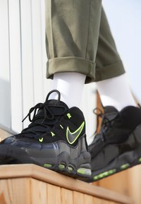Černé tenisky Nike mají lesklý povrch, neonově zelené akcenty a design na šněrování. Viditelné Air odpružení umístěné na podrážce.