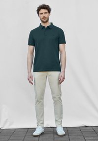 Mörkgrön polo skjorta med korta ärmar, två-knapps placket, ihop med ljusbeige slim-fit byxor och vita sneakers.