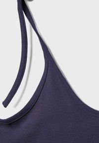 Gros plan d'un top bleu marine à fines bretelles montrant la texture du tissu et les détails des coutures sur un fond clair.
