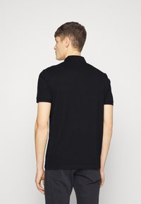 Polo noir avec col, manches courtes et ourlet droit. Fabriqué en tissu lisse, au design minimaliste sans motifs ni accents.