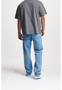 T-shirt grigio in cotone a maniche corte abbinato a jeans in denim blu chiaro. I jeans hanno una vestibilità comoda con un leggero sbiadimento e due tasche posteriori.