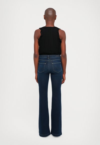 Svart ärmlös blus med volanger på axlarna, kombinerad med mörkblå utställda jeans. Jeansen har standardfickor och en något urtvättad textur.