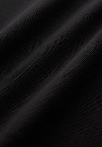 Tessuto nero con una superficie strutturata, che mostra un motivo intrecciato. Il materiale appare resistente e leggermente riflettente sotto la luce.