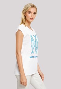 White cotton t-shirt with short sleeves, featuring blue fish graphics and "SALTY BUTS" text in a casual font. Simple, relaxed design.
