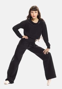 Svart långärmad topp och vida byxor tillverkade av mjukt, flexibelt tyg. Notabelt cropped mönster vid midjan och minimalistisk logotypdetalj.