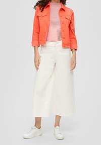 Korallfärgad denimjacka, randig topp i röd och vit, vita vida jeans, vita sneakers med snörning och en strukturerad yta. Avslappnad klädensemble.