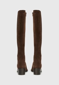 Bottes en daim marron jusqu'au genou avec une forme ajustée, fermeture éclair sur le côté et un talon carré bas pour plus de stabilité. Texture lisse et design minimal.