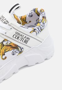 Sneaker Versace Jeans Couture με λευκό συνθετικό άνω μέρος, πολύχρωμο σχέδιο λουλουδιών στο εσωτε�ρικό καιrobust λευκή σόλα με υφή.