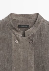 Bruine textuurstof blouse met een mandarijnkraag en twee zichtbare knopen bij de halslijn, label met de tekst "Massimo Dutti."