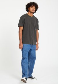 Grijze katoenen t-shirt met een ronde hals, gecombineerd met blauwe losse denim jeans en zwarte canvas sneakers.