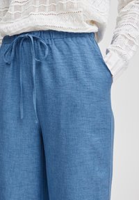 Pantaloni in tessuto leggero di colore azzurro, con vita elastica e dettagli con cordoncino, dotati di tasche laterali e una vestibilità comoda.