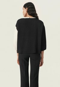 Haut bicolore noir et crème à coupe ample, avec des manches trois-quarts et un petit détail de fermeture éclair dans le dos. Associé à un pantalon noir.