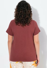 Camiseta corta de manga maroon con un corte relajado, que presenta un cuello redondeado y una textura suave, combinada con pantalones de estampado floral.