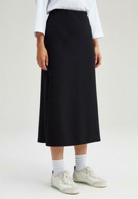Svart midi kjol med slät tyg, rak silhuett, elastisk midja och subtila sömmar på sidan, matchad med vita sneakers.