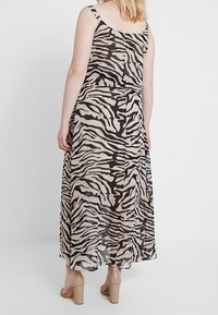 Robe longue avec imprimé zèbre noir et beige, confectionnée dans un tissu léger et transparent, dotée de bretelles réglables et d'une silhouette fluide.