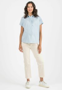 Camicetta azzurro chiaro a maniche corte con strisce bianche, colletto con bottoni e dettaglio a pieghe. Abbinata a pantaloni cropped color crema e sneaker bianche.