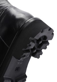 Black leather boot showing textured rubber sole with prominent grip patterns. Upper has smooth finish and slightly raised seam detail.