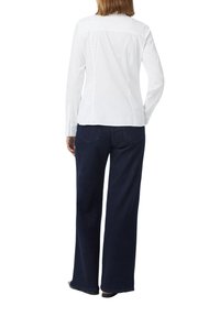 Weißes Langarmbluse mit einer taillierten Silhouette, kombiniert mit weit geschnittenen dunkelblauen Jeans. Die Rückseite zeichnet sich durch ein einfaches Nahtdesign aus.