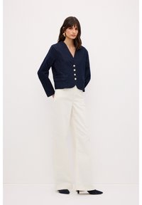 Chaqueta de mezclilla navy recortada con escote en forma de V y cierre de botones dorados, combinada con pantalones de pierna ancha color crema y tacones negros de punta.