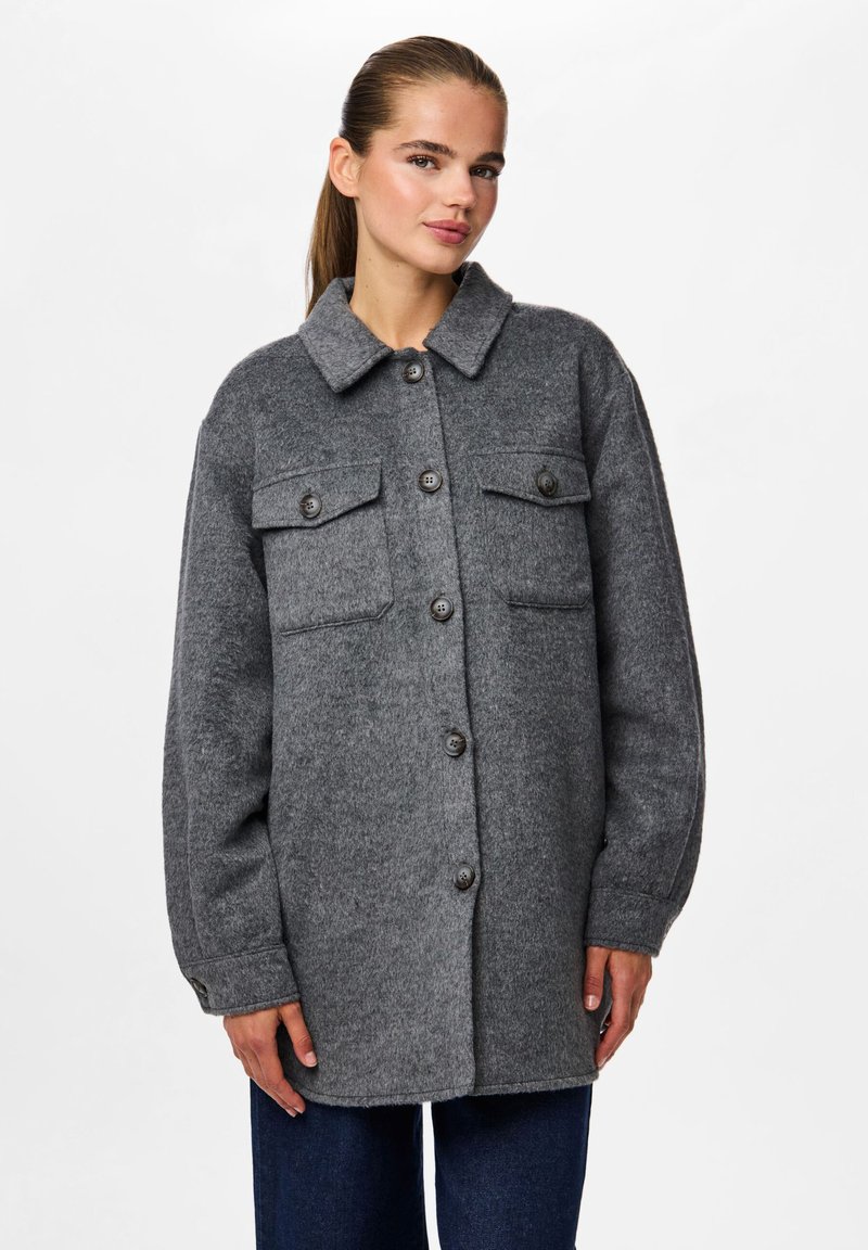 Γκρί μάλλινο σακάκι με γιακά, δύο τσέπες στο στήθος και κουμπιά μπροστά. Διαθέτει μακρύ μανίκι και έντονη εφαρμογή.