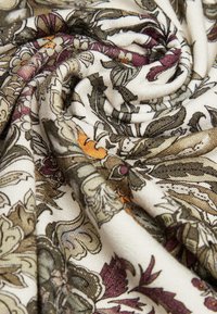 Stoff mit floralem Muster auf cremefarbenem Grund. Zeigt sanfte Grüns, Purpurtöne und goldene Fäden und präsentiert eine glatte, strukturierte Oberfläche.