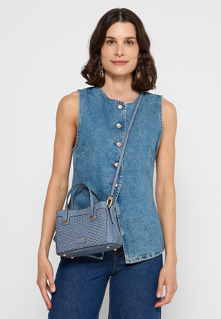 Veste en denim avec une fermeture à boutons à l'avant, un col rond et sans manches. Accompagnée d'un petit sac à main tissé bleu avec des poignées courtes.