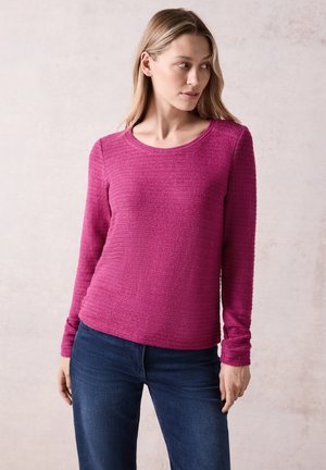 Haut fuchsia à manches longues en tissu texturé avec des rayures horizontales, présentant un col rond et une silhouette ajustée. Équilibre avec un jean noir.