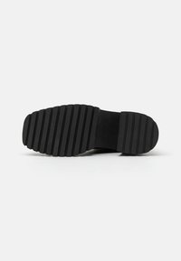 Musta kuminen kengänpohja, jossa syvät vaakasuorat urat pidon parantamiseksi. Varvas- ja kantapääalueet hieman kaarevat, sileä viimeistely.