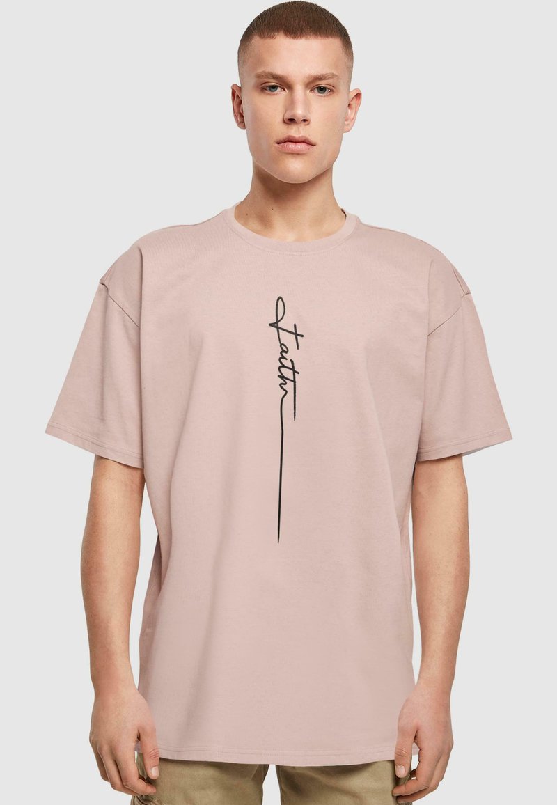 Camiseta de manga corta de color rosa claro, hecha de algodón. Presenta un diseño gráfico negro con la palabra "fe" alineada verticalmente en el centro.