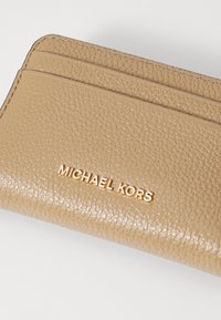 Bežna teksturirana uslužna torbica za kartice z več režami in zlatim logotipom "MICHAEL KORS". Gladka površina z zašitimi robovi. Kompaktna zasnova.