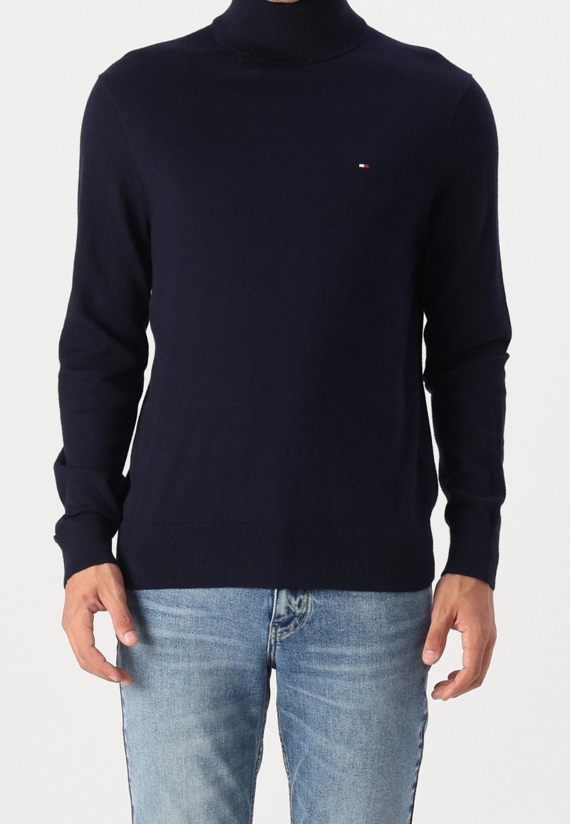 Marinblå polo-tröja i mjukt material med långa ärmar och ribbade muddar. Litet logotypdetalj på bröstet. Kombinerad med ljusblå jeans.