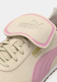Lys beige semsket sneakers med rosa aksentstripe og gummisåle. Har polstret tunge med preget logo og flate lisser.