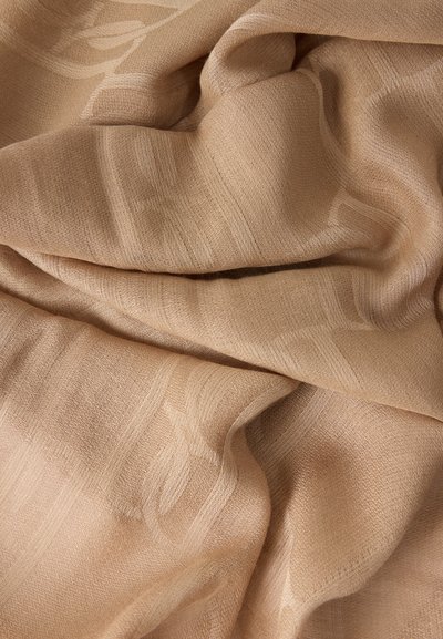 Μπεζ ύφασμα με λεπτά υφασμένα γεωμετρικά σχέδια και απαλά πτυχώματα που δημιουργούν απαλή σκιά και φωτεινές ανταύγειες.