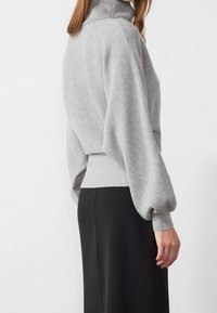 Maglione grigio con colletto alto, texture a coste e maniche a palloncino. Abbinato a un tessuto nero liscio, creando un look a strati.