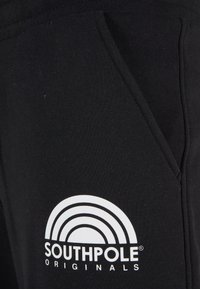 Czarne dresy z przednią kieszenią i białym logo z nadrukiem, które przedstawia tęczowy wzór oraz napis "SOUTHPole ORIGINALS."