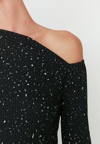 Svart off-shoulder topp med ribbad textur, prydd med spridda vita prickar. Mjuk tyg med elastisk halsringning och strukturerad passform.