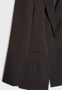 Tmavě hnědý blazer se strukturovanými ramenními vycpávkami, zapínání na jeden knoflík a dvěmi šikmými kapsami vpředu. Hladká tkanina s přiléhavým střihem.