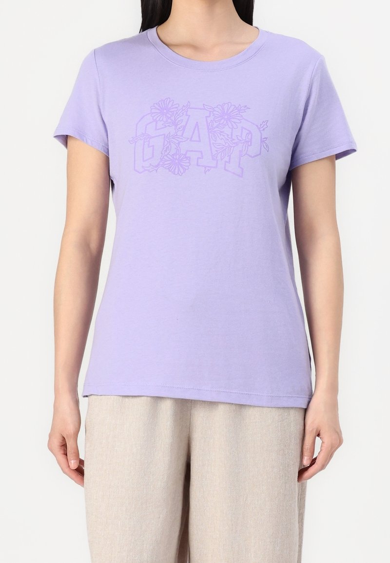 T-shirt en coton lavande avec logo GAP et accents floraux. Manches courtes et encolure ras du cou. Texture douce, coupe décontractée.