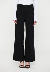 Pantaloni neri a gamba larga realizzati in un tessuto robusto, con vita alta, tasche frontali e chiusura con bottone argento. Abbinati a sandali neri.