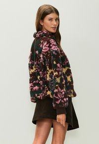 Mäkká mikina s kvetinovými vzormi v ružových, zelených a bordových odtieňoch, s vysokým golierom a textúrovaným povrchom.