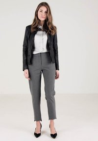 Svart läderjacka över en vit blus, kombinerad med grå skräddarsydda byxor och svarta spetsiga klackskor. Släta texturer, skräddarsydd design.
