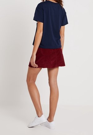 Marineblå bomulds t-shirt med en afslappet pasform, sammen med en struktureret bordeaux-rød fløjlskørt. Hvide sneakers fuldender outfittet.