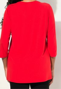 Tunic rossa a maniche lunghe con vestibilità comoda, caratterizzata da un collo rotondo e una texture liscia e morbida. Abbinata a leggings neri.