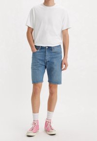 Pantalones cortos de mezclilla en azul claro con corte recto, bolsillos frontales y cierre de botón, combinados con una camiseta blanca y zapatillas rosas de caña alta.